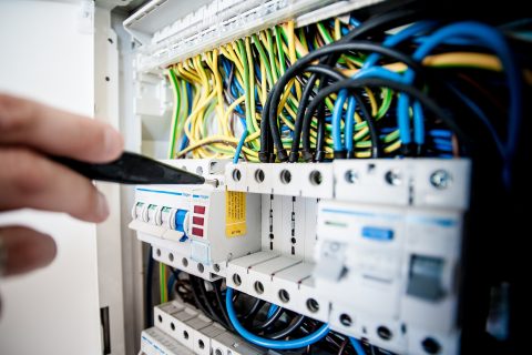 Eine Hand arbeitet mit einem schwarzen Phasenprüfer an Leitungen in einem Sicherungskasten.